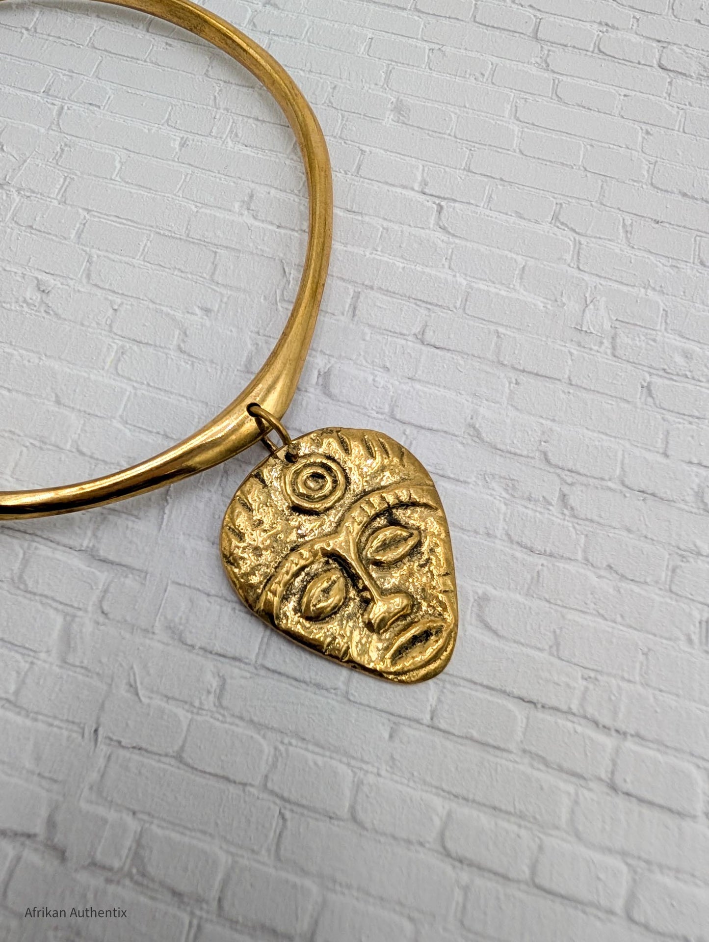 gold collar necklace with an African mask pendant on a textured gray background