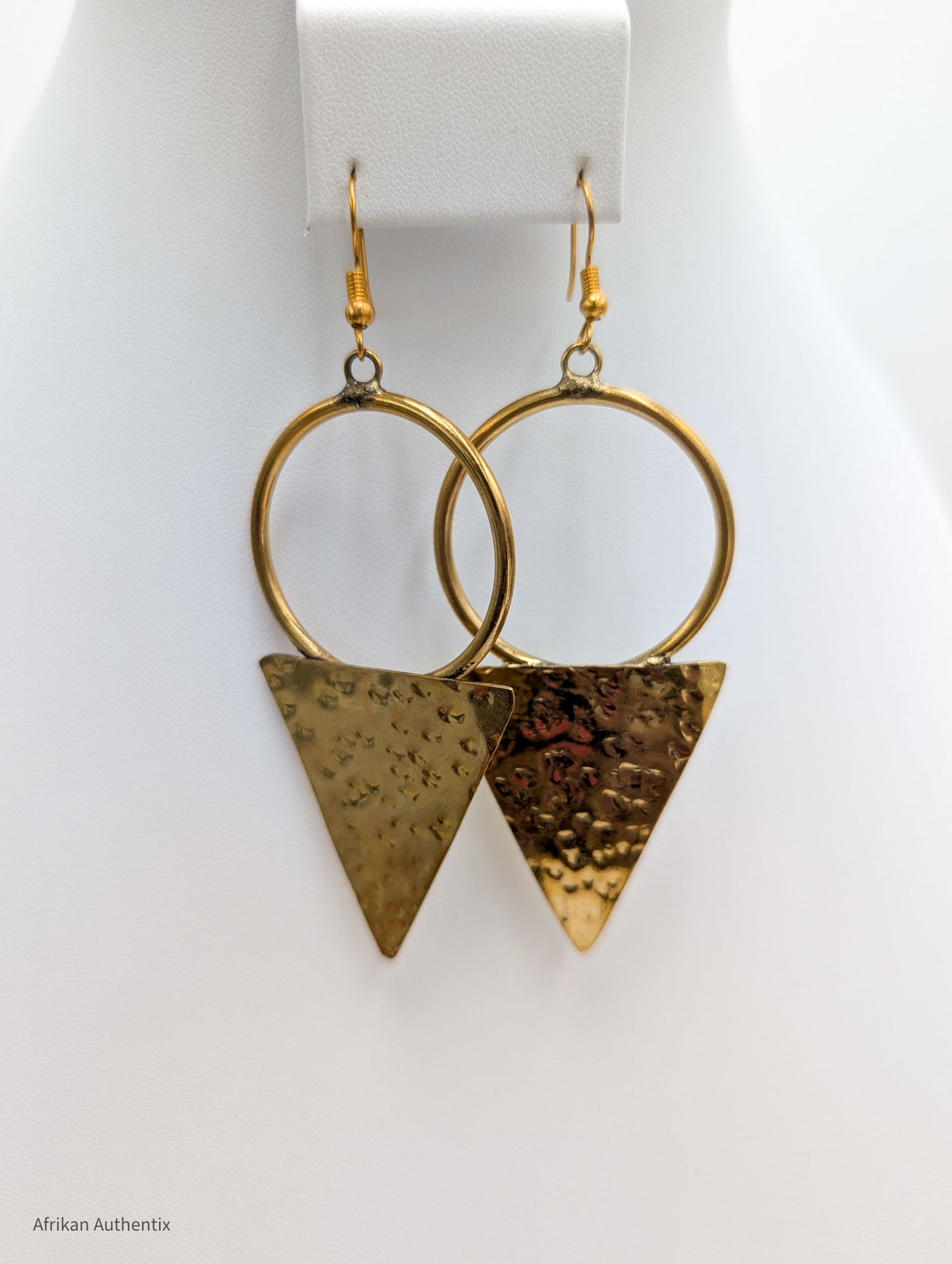 Hammered brass triangle and hoop earrings displayed on white jewelry stand