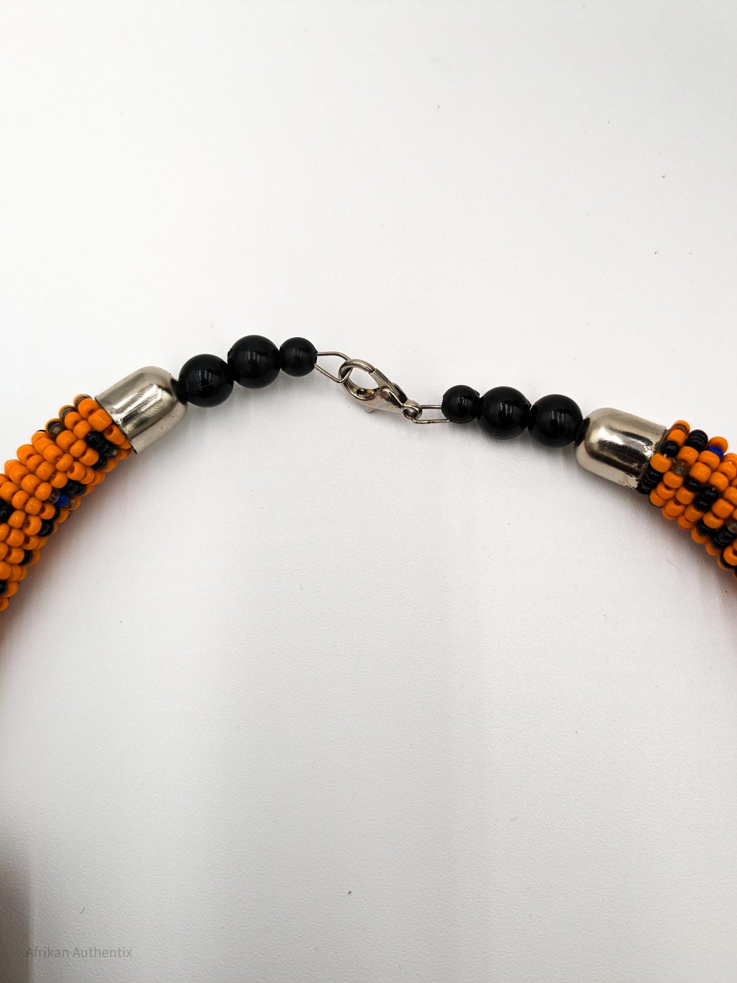 Close-up of a Kenyan beaded necklace with orange, black beads, silver caps, and a metallic clasp on a white background