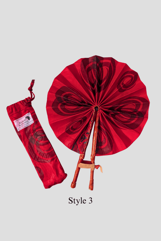 Red African hand fan with black swirl patterns and wooden handles alongside matching fabric pouch labeled Made in Ghana
