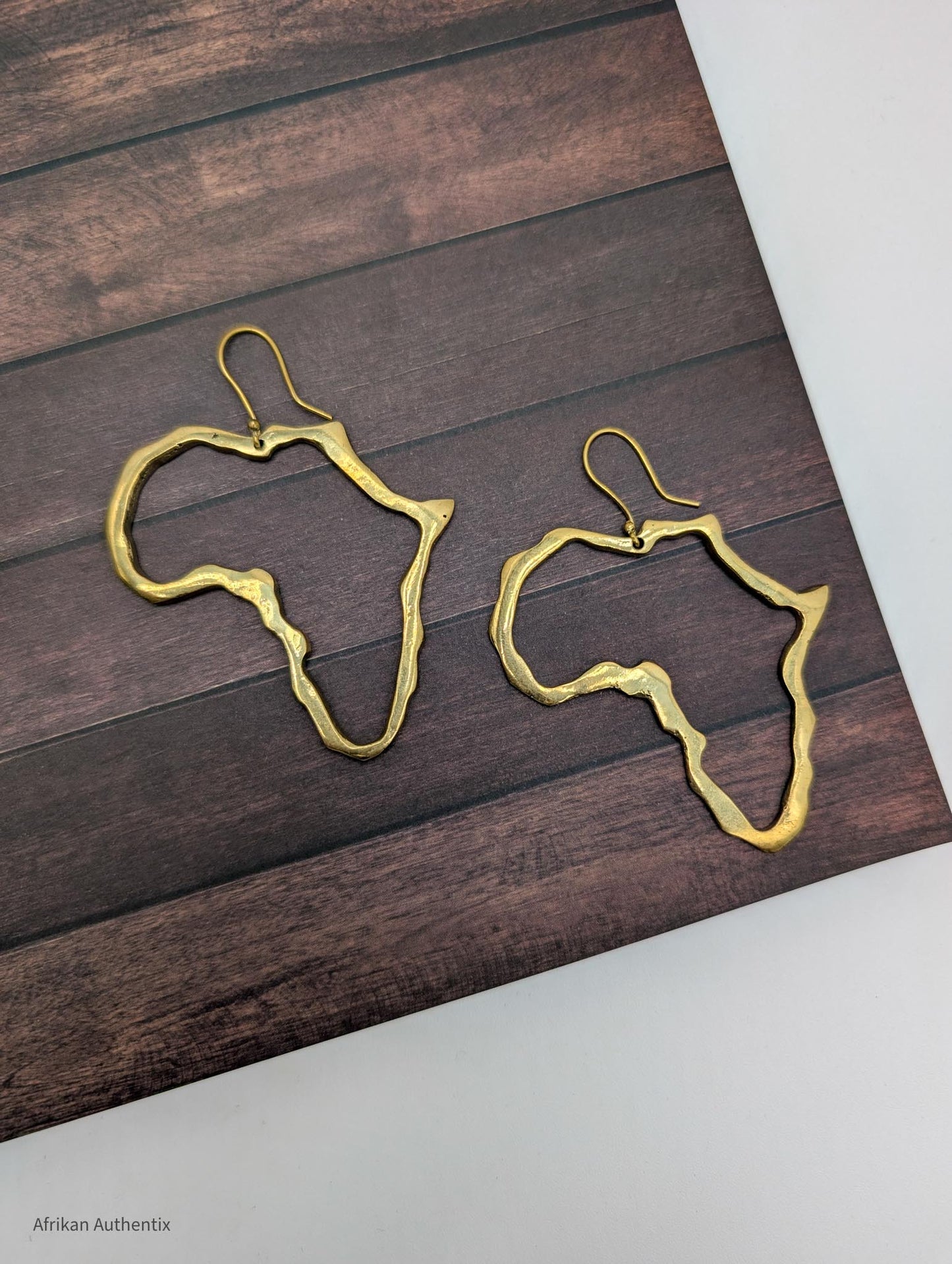 Gold Africa outline earrings on a wooden surface