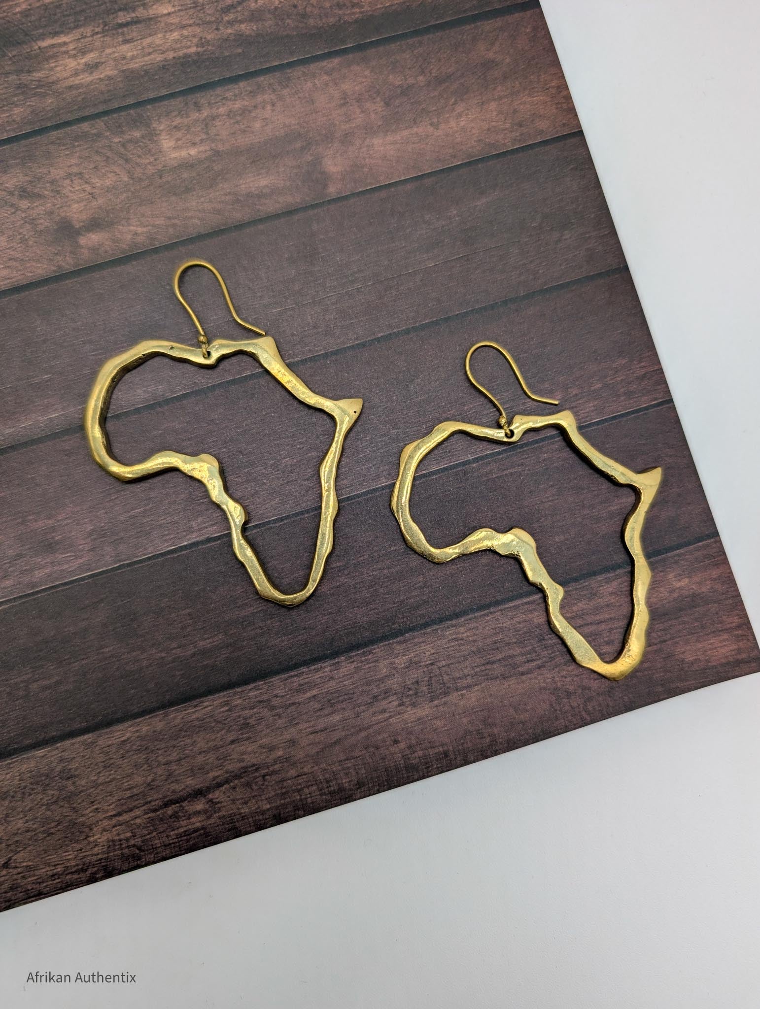 Gold Africa outline earrings on a wooden surface