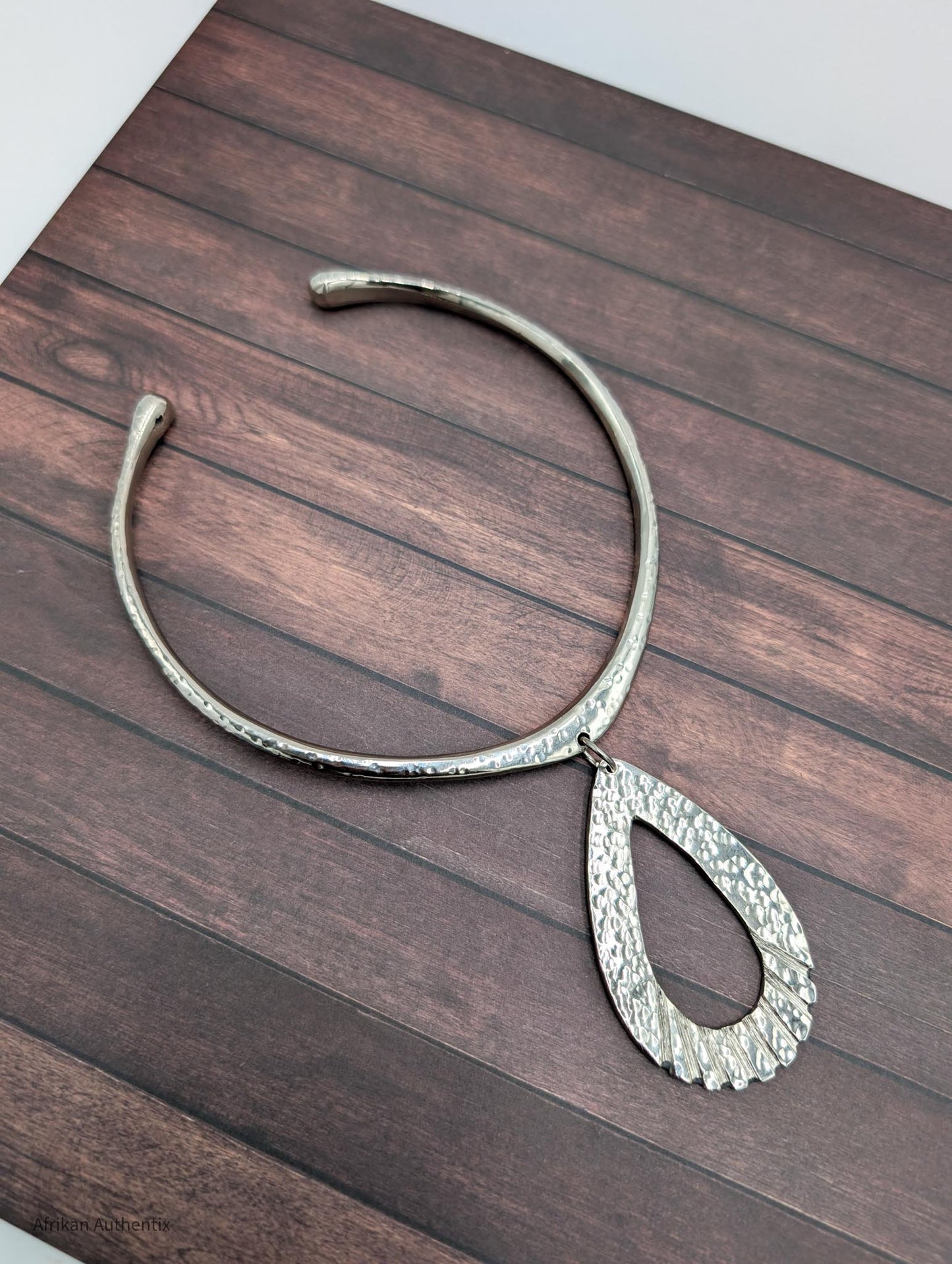Silver collar necklace with a teardrop pendant on a wooden surface