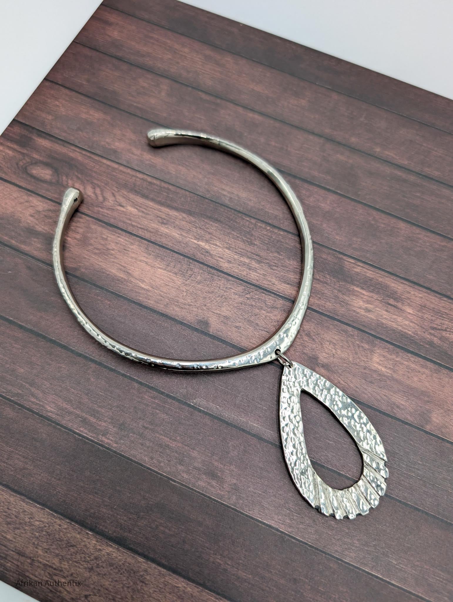 Silver collar necklace with a teardrop pendant on a wooden surface