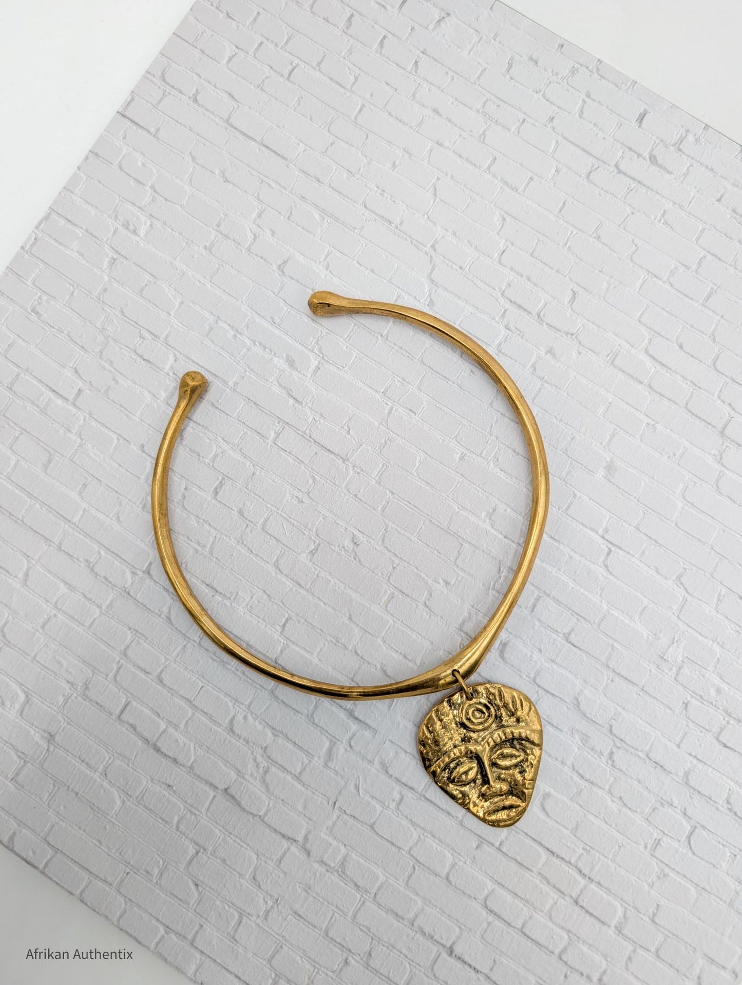 gold collar necklace with an African mask pendant on a white brick background