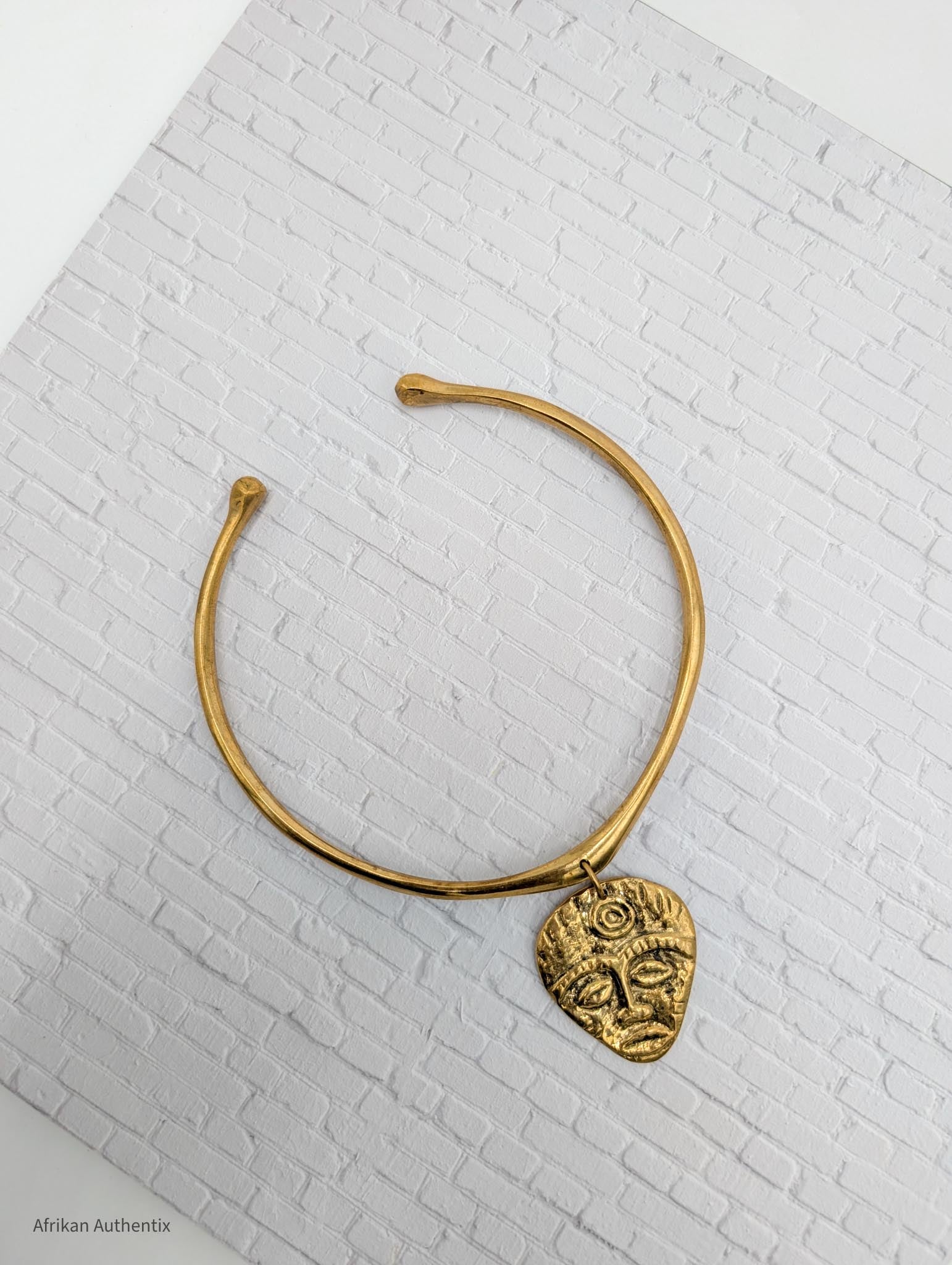 gold collar necklace with an African mask pendant on a white brick background