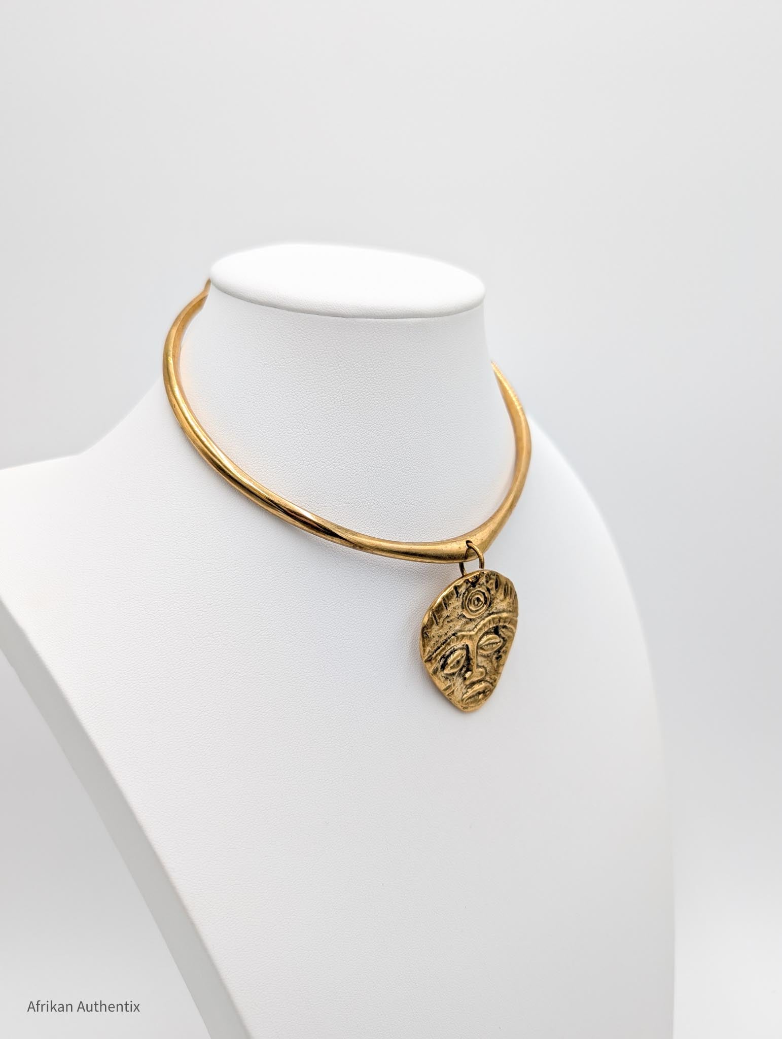 old collar necklace with an African mask pendant on a mannequin bust against a white background