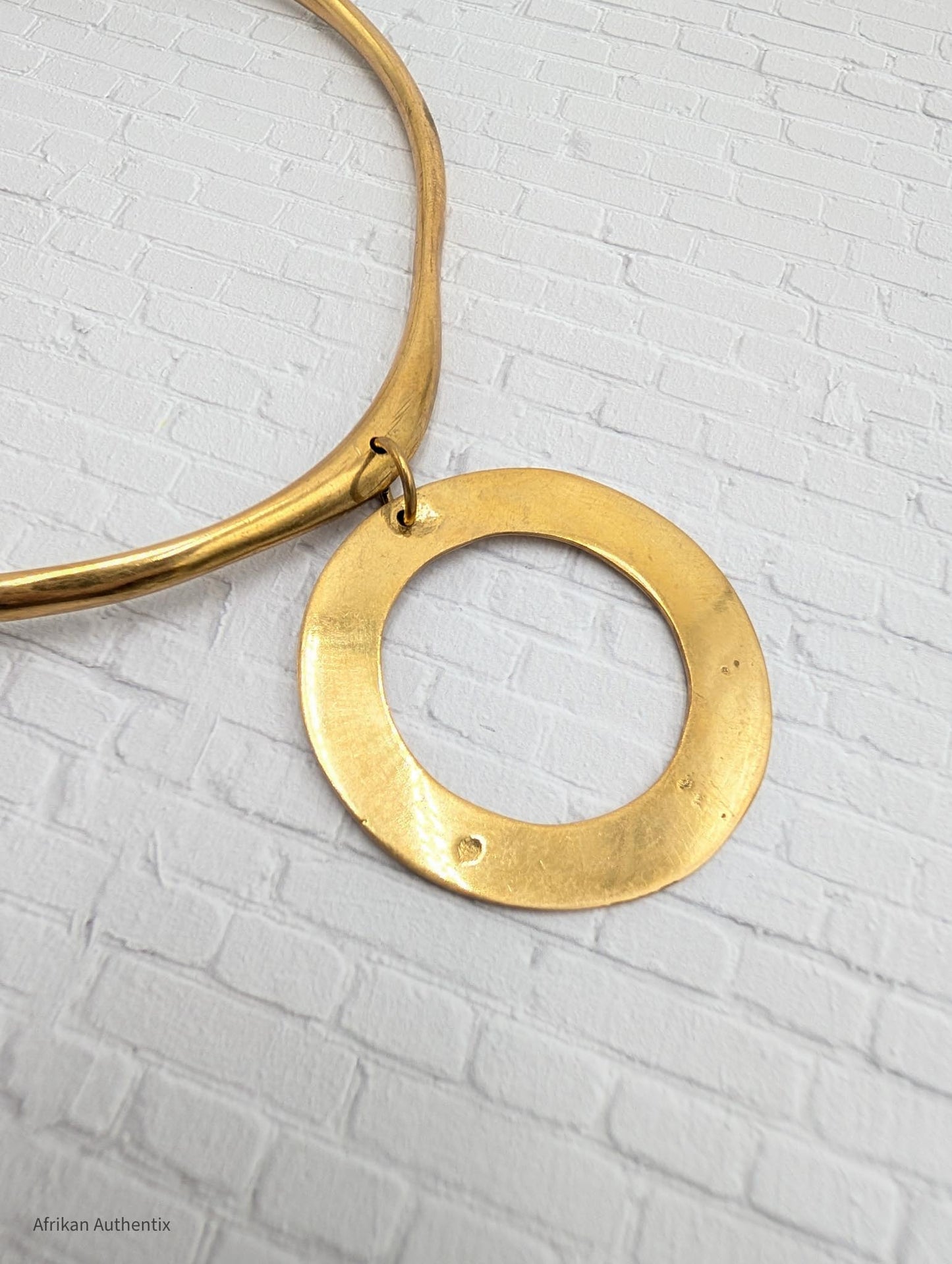 a brass collar necklace with a circular pendant on a textured white background