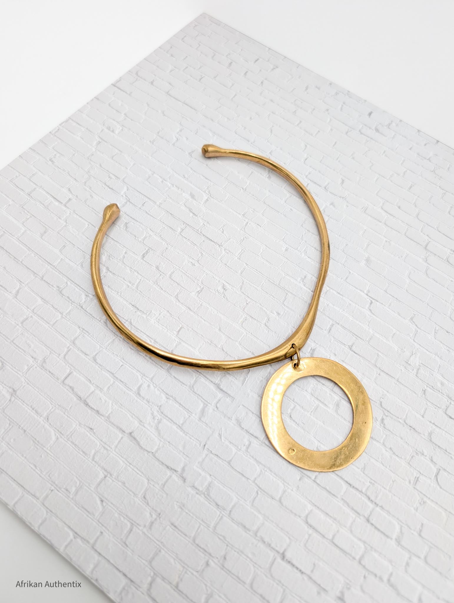a brass collar necklace with a circular pendant on a textured white surface