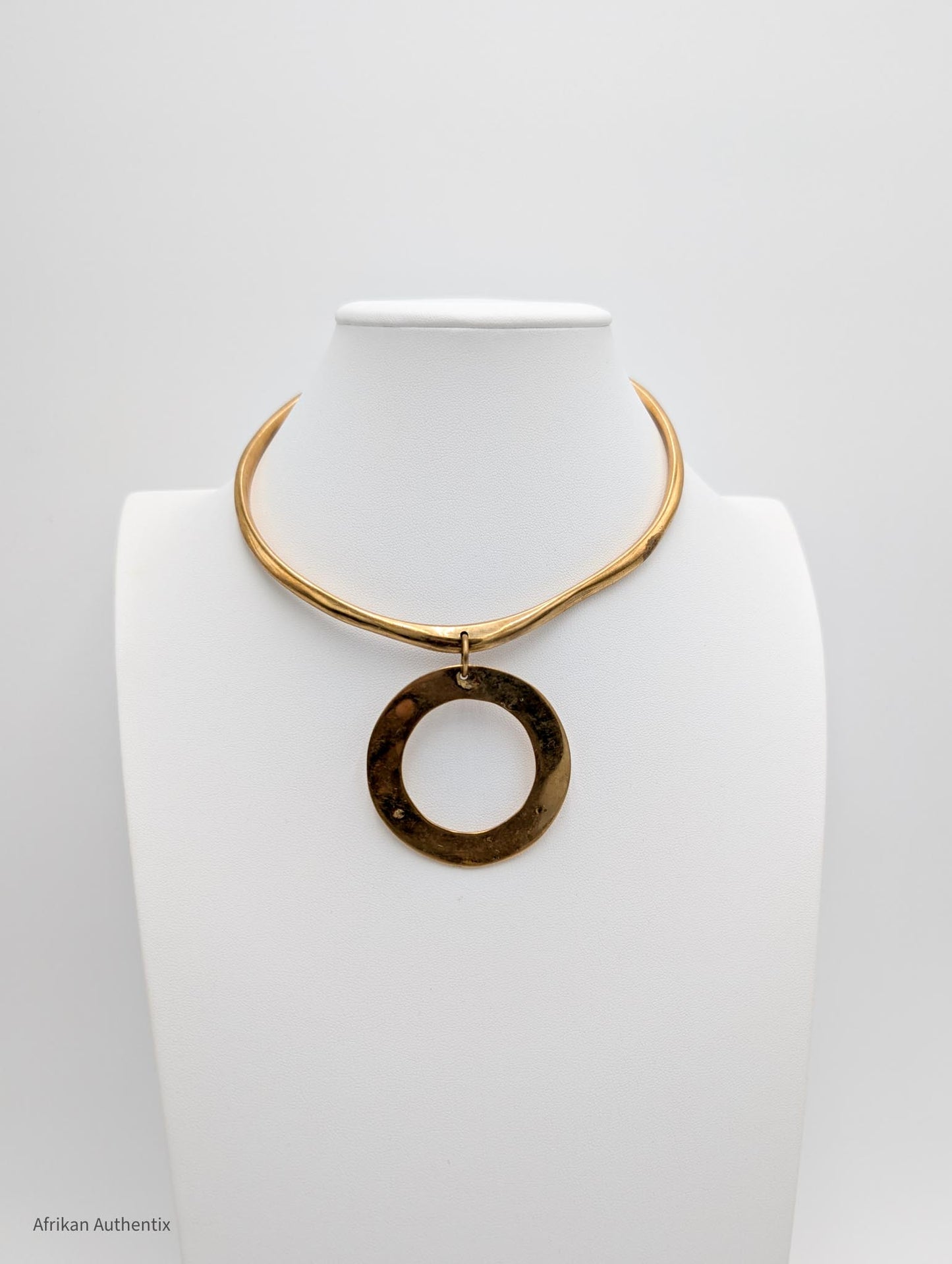 a brass collar necklace with a large circular pendant on a white mannequin bust.