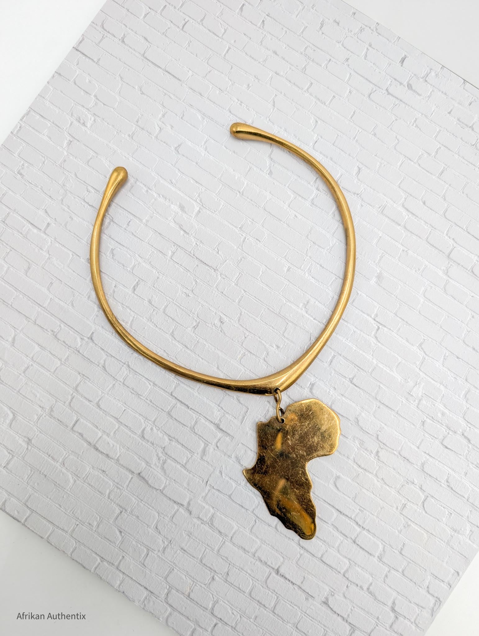 Gold collar necklace with an africa map pendant on a white brick background