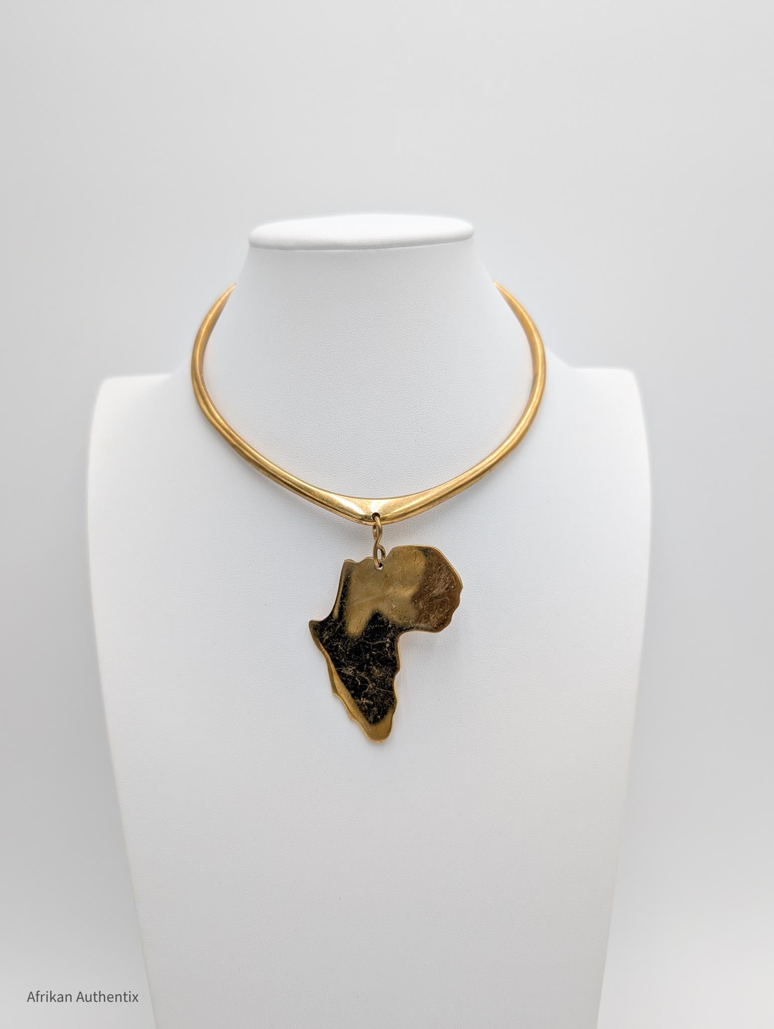 Gold collar necklace with an africa map pendant  on a white mannequin against a gray background