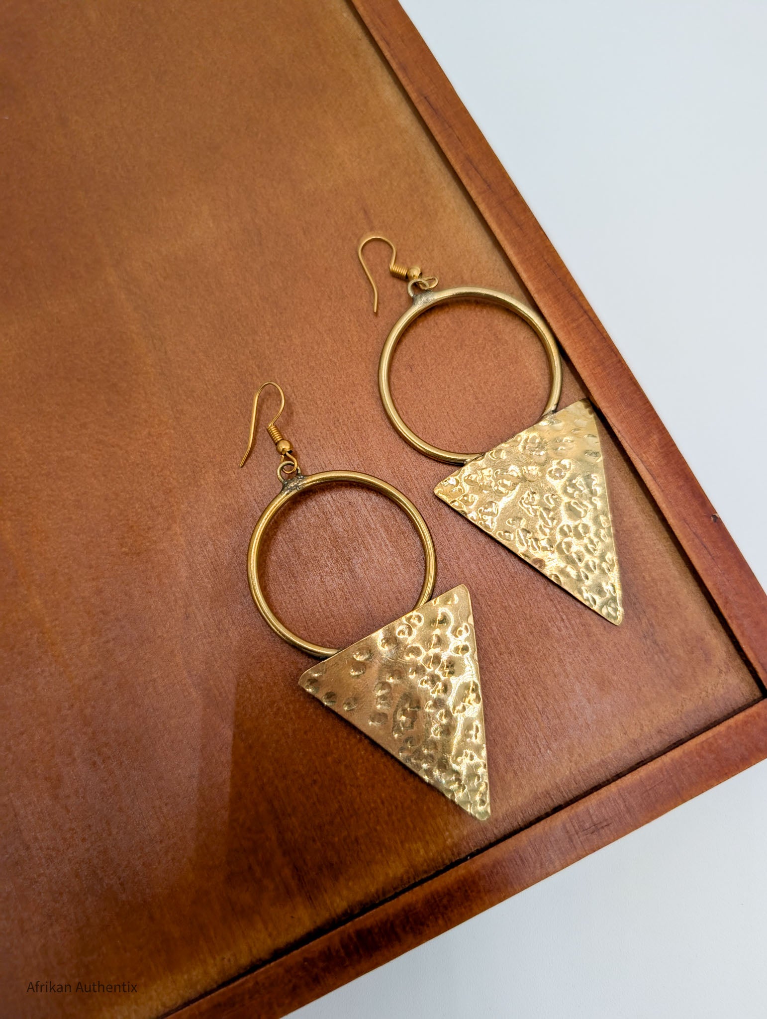 Hammered brass triangle and hoop earrings displayed on white jewelry stand