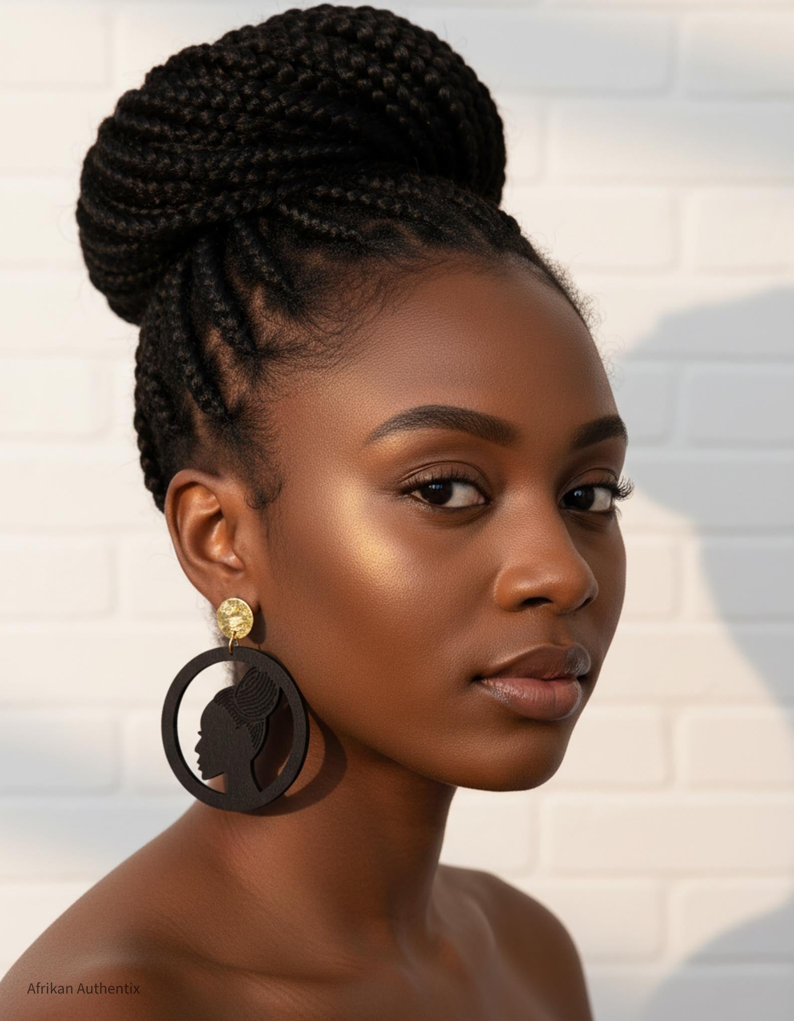 Woman with braided hair styled in an updo, wearing an african woman silhouette earrings against a neutral background.