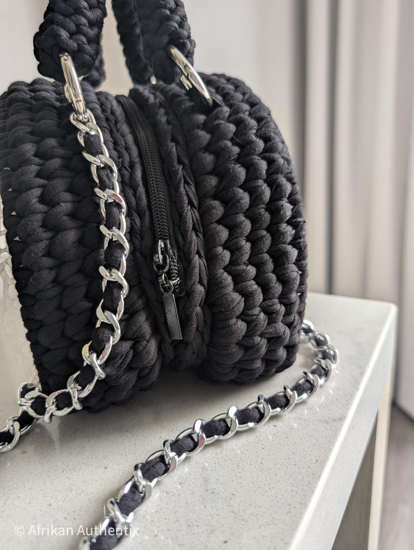 Black woven handbag with silver chain strap on a light surface by Afrikan authentix