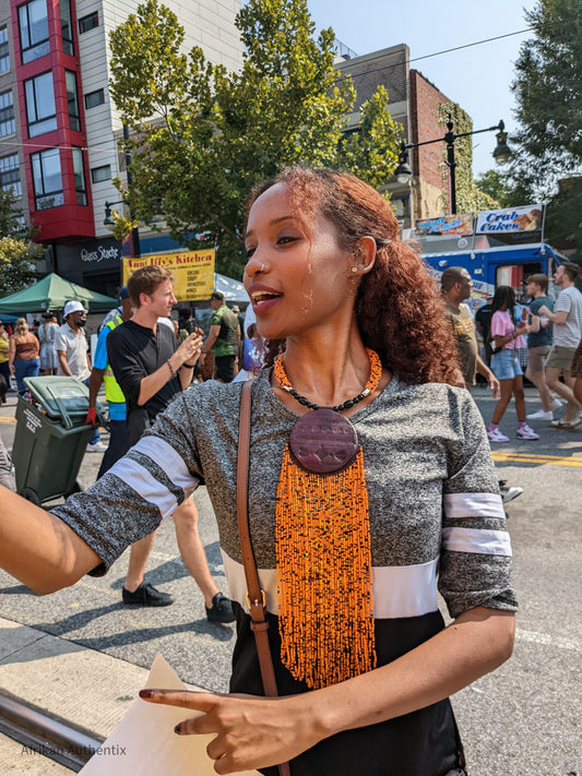 Woman at outdoor market wearing gray top and handmade orange beaded necklace with large brown pendant
